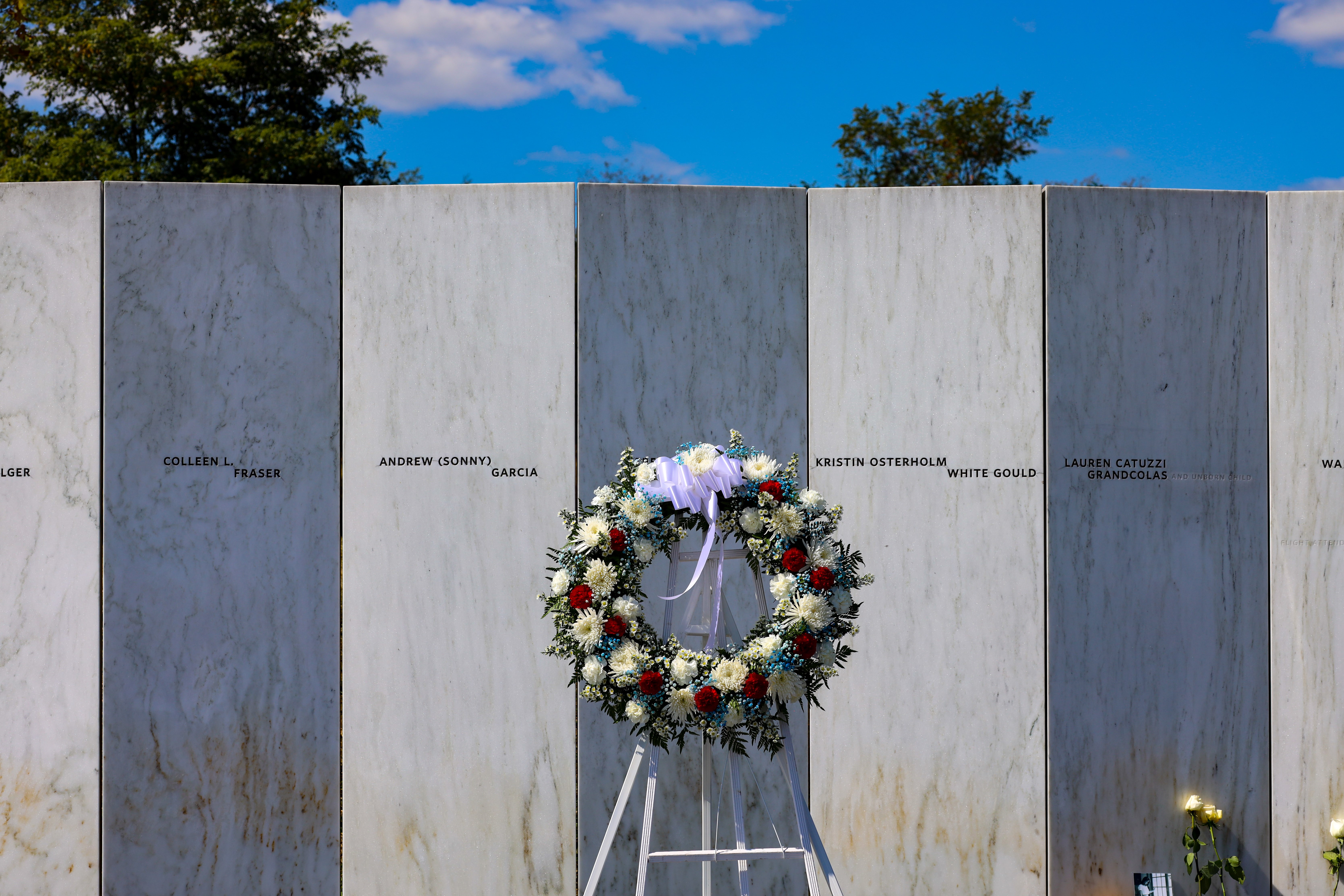 A wreath stands in front of the white marble wall of names
