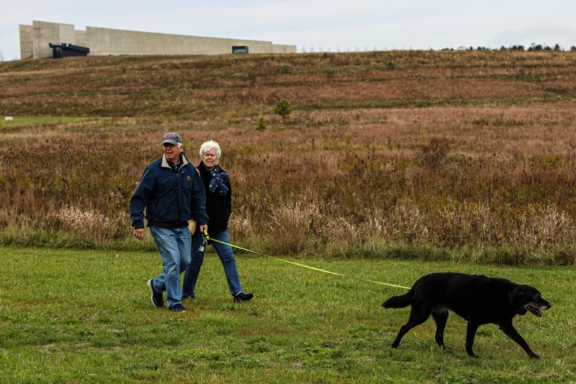 Visitors walking with their leashed dog on a trail.