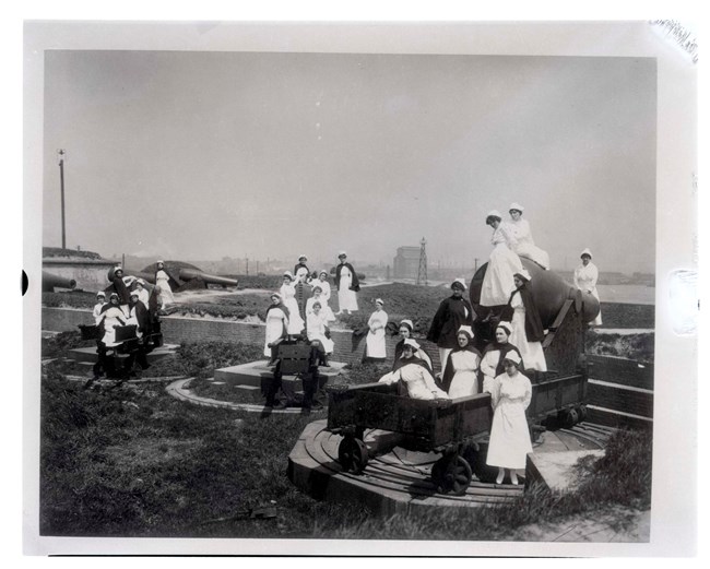 A black and white image of a group of nurses posing on top of Rodman cannons in the outer battery of Fort McHenry.