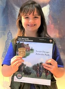 A girl holding the Fort Necessity Junior Ranger booklet and badge