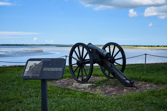 A historic cannon with large wheels faces into the harbor