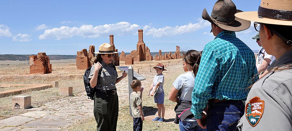 Female ranger speaking to visitors in front of adobe ruins
