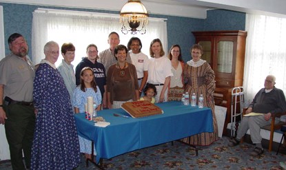 Image of staff and volunteers standing around a cake commemorating the McLoughlin House Site's third anniversary