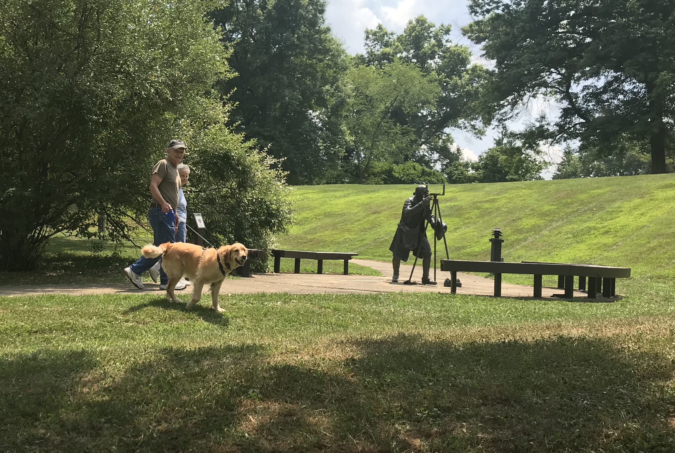 Couple hiking with dog near statue of Albert Gallatin