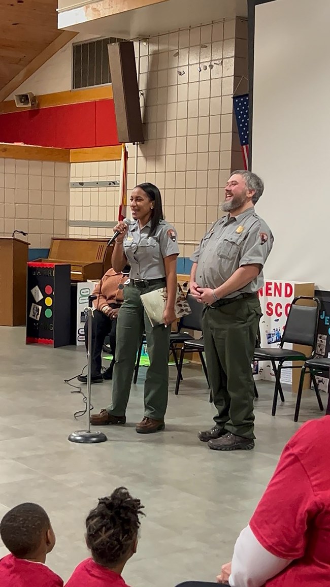Two rangers stand in front of a group of students and teachers.