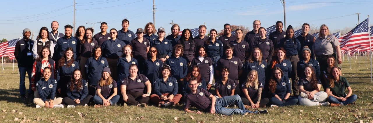 A group photo of Community Volunteer Ambassadors members posing in front of a USA flags while wearing navy blue polos with the official Community Volunteer Ambassador logo.