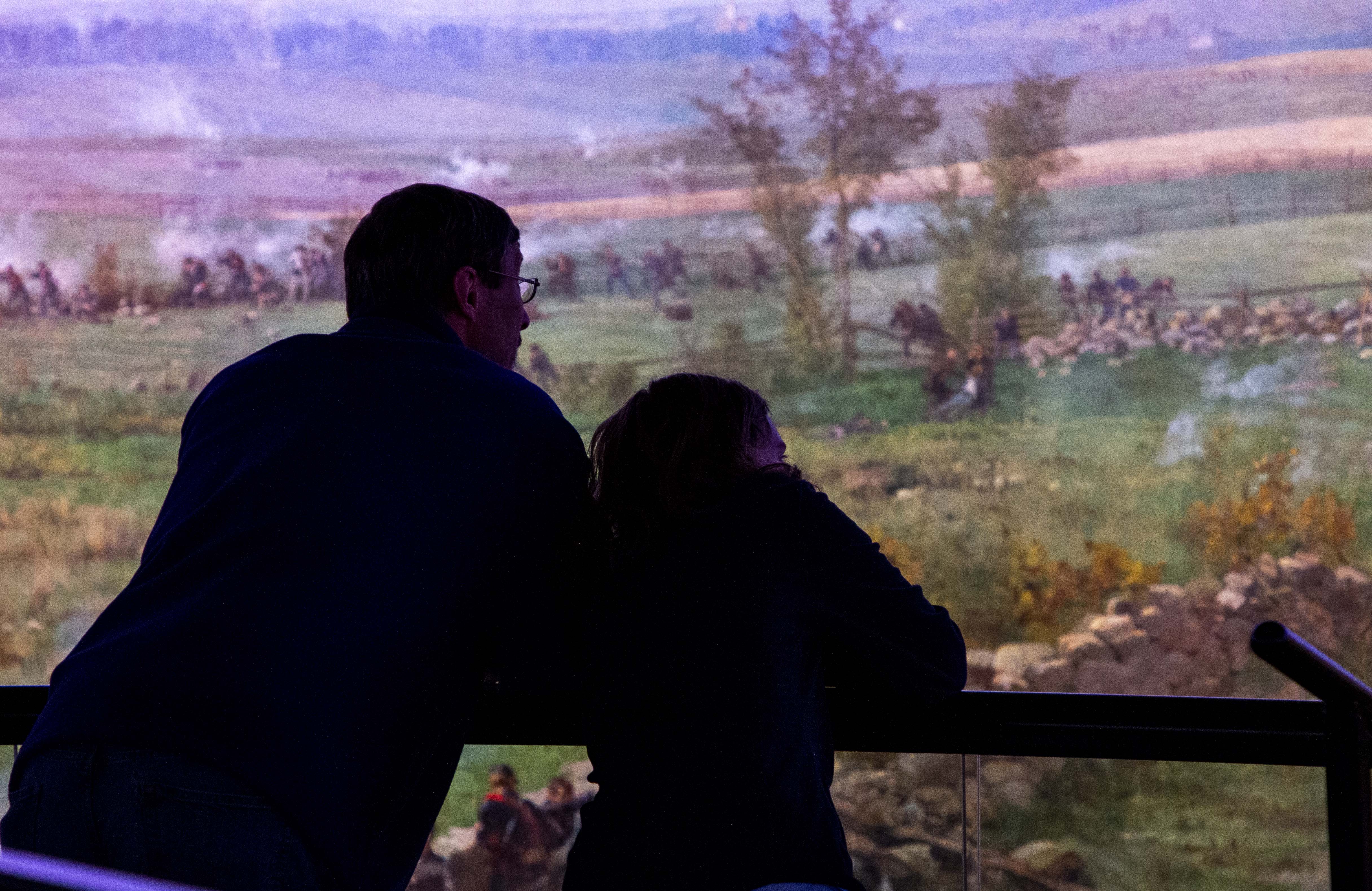 A father and child stand silhouetted in front of a large colorful painting.