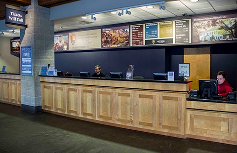 Staff operate the ticket desk. There are staff seated behind a long counter with colored signs behind them describing tours and costs.