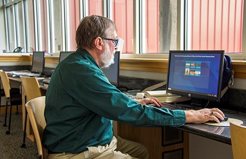 A park volunteer sits at a computer in the McKenna Foundation Resource Room ready to help visitors with their research questions.