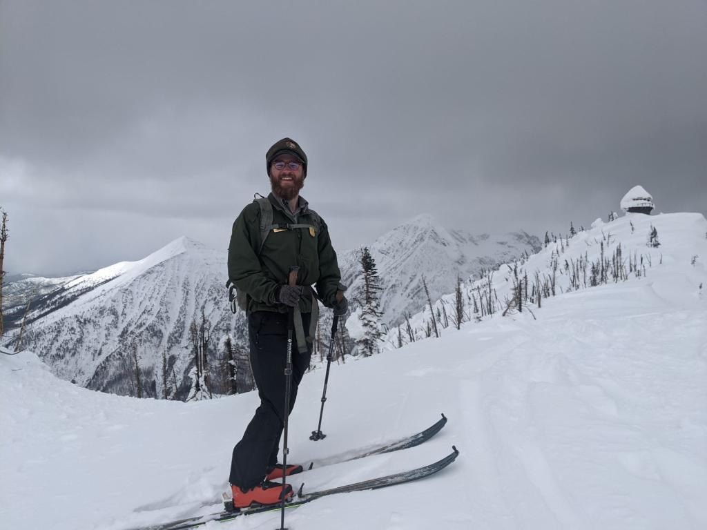 A park ranger cross country skis on a snowy mountain