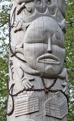 a featureless face with several hands carved into a totem pole