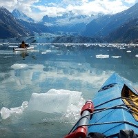 two kayakers in blue waters near a glacier and mountains