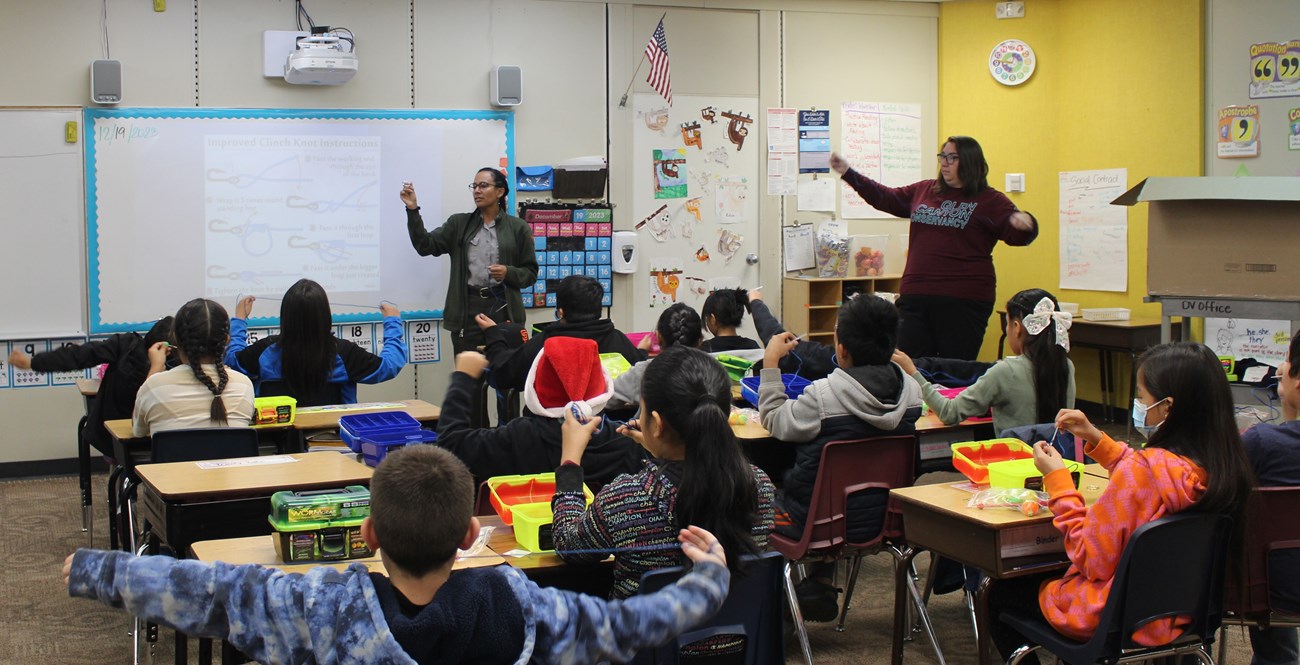 Two park rangers at the head of a classroom demonstrate how to tie fishing line.