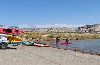 Two men stand in water at end of launch ramp with a stack of kayaks