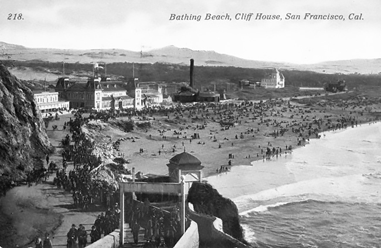 historic postcard showing long, crowded beach with amusement park buildings in the background.