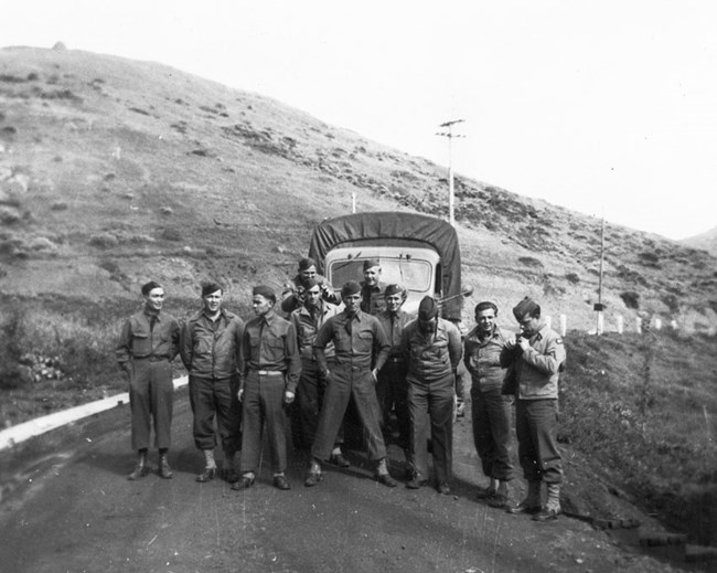a group of soldiers at ease, standing in front of a truck