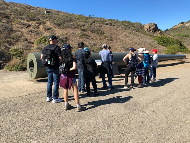 Group of visitors stand infront of the 16 inch gun while a Volunteer in Parks (VIPs) leads them on a tour