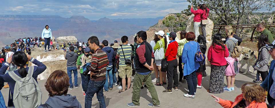 a crowd of people wearing a variety of colorful clothing, on an upper level of Mather Point scenic overlook.