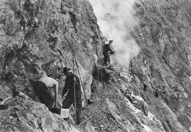 Three workers carving the cliff into a trail