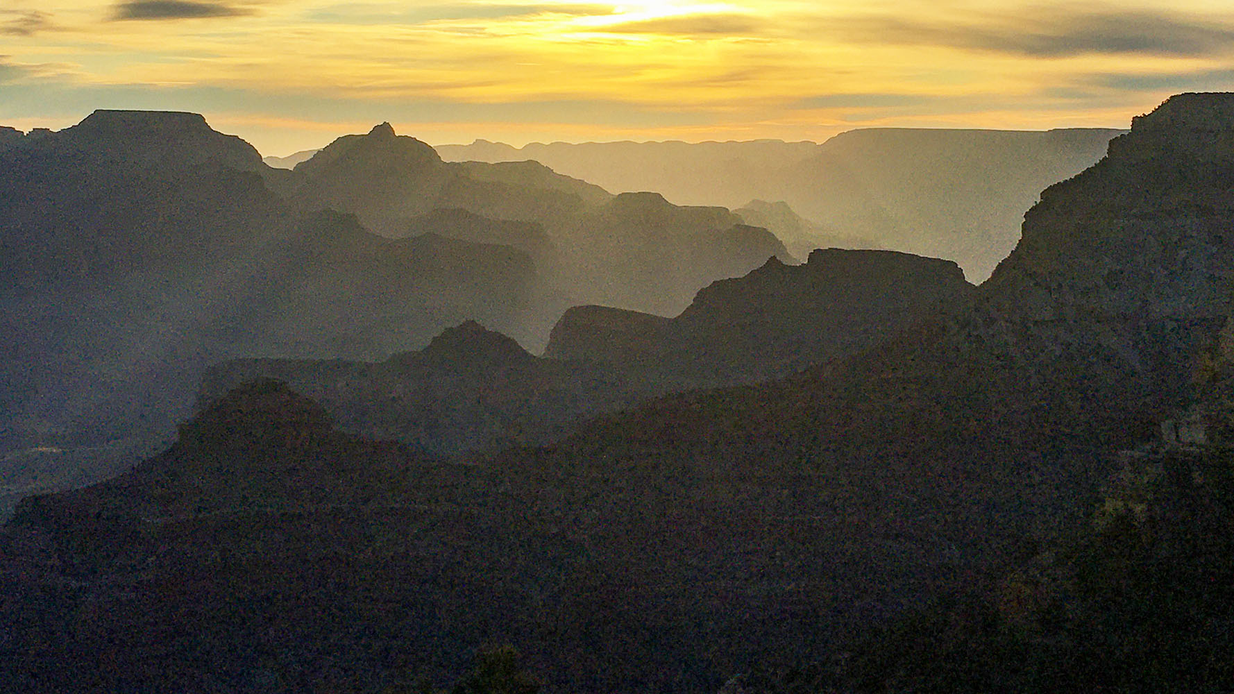 a series of silhouetted ridgelines and promontories bathed in yellow sunrise light.