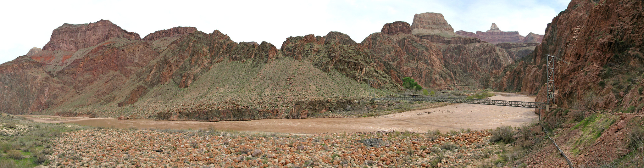 A trail linking to a large bridge spanning across the Colorado River with tall canyon walls on either side.