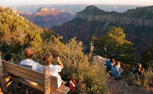 A group of people watching sunset from an overlook at the south end of the campground. Several are sitting on a bench on the left. Others are sitting on a ledge below and to the right.