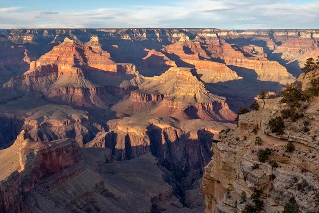 Within a vast canyon landscape, colorful cliffs and peaks are becoming engulfed by evening shadows.