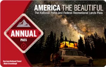 The 2022 Interagency Annual Pass with a 4-wheel drive vehicle with a tent on top under a starry night sky.