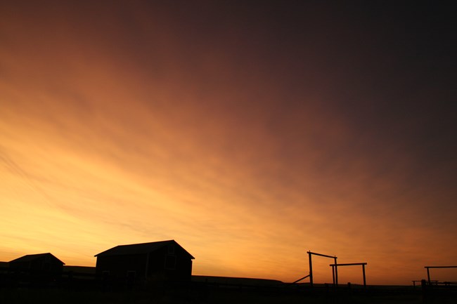 Sunset sky with silhouette of barns and gate arches.