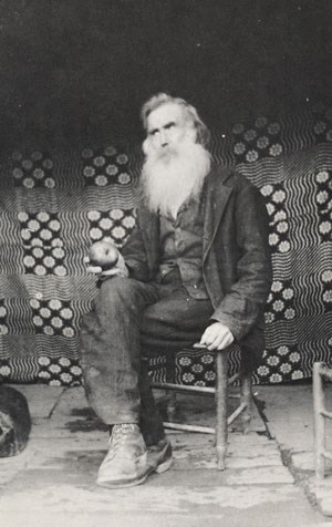 John Walker sits on a wooden chair with an apple in his hand