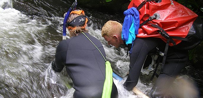 Two scientists in wet suits searching for hellbender salamanders in a fast flowing river