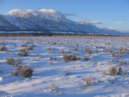 Lenticular clouds hover over the Teton Range, windswept snow and sagebrush in the valley below.