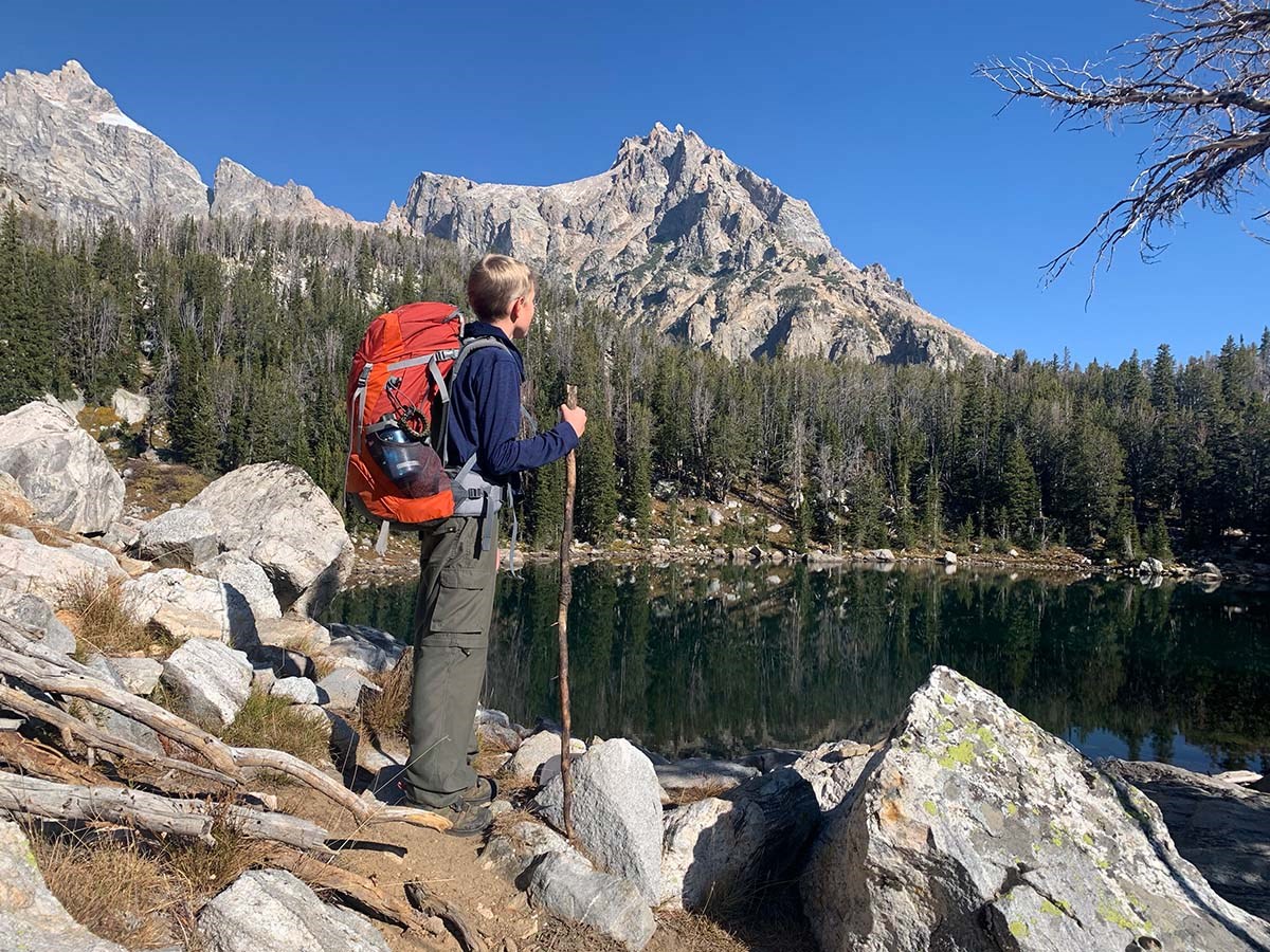 Hiker with backpack standing on the edge of a alpine lake with peaks in the distance