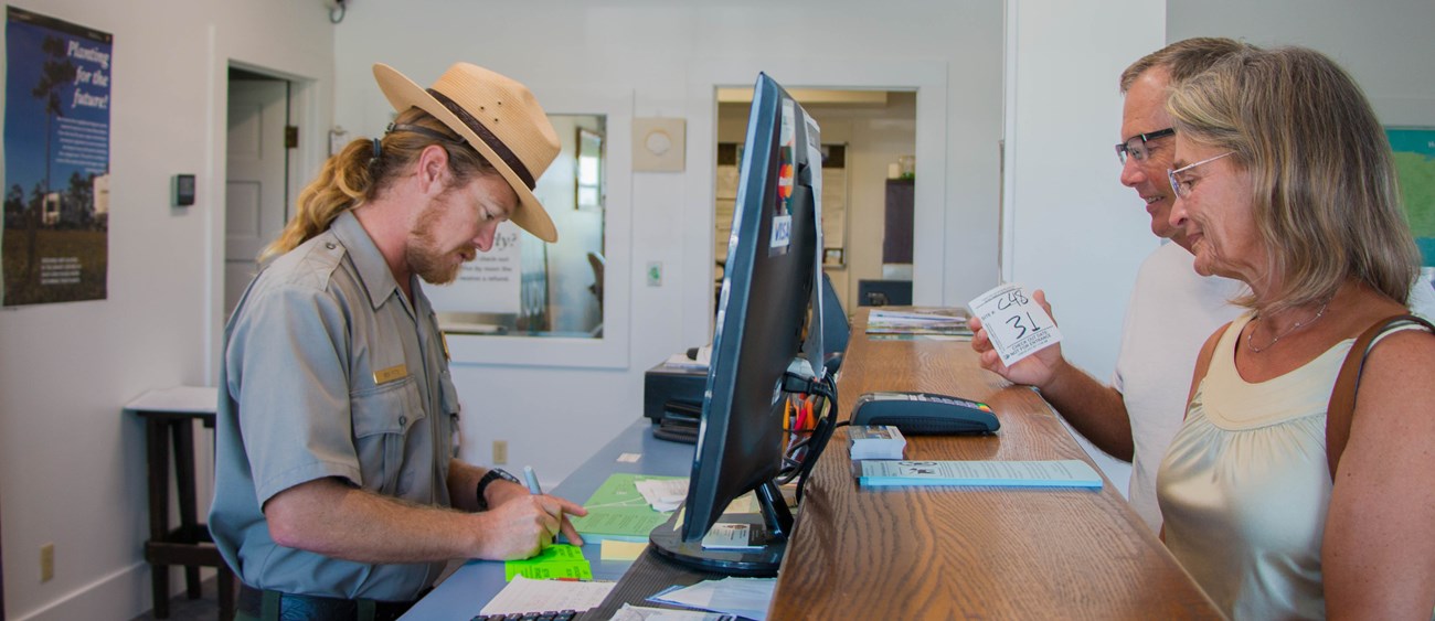A ranger stands at a desk checking in a couple to the campground.