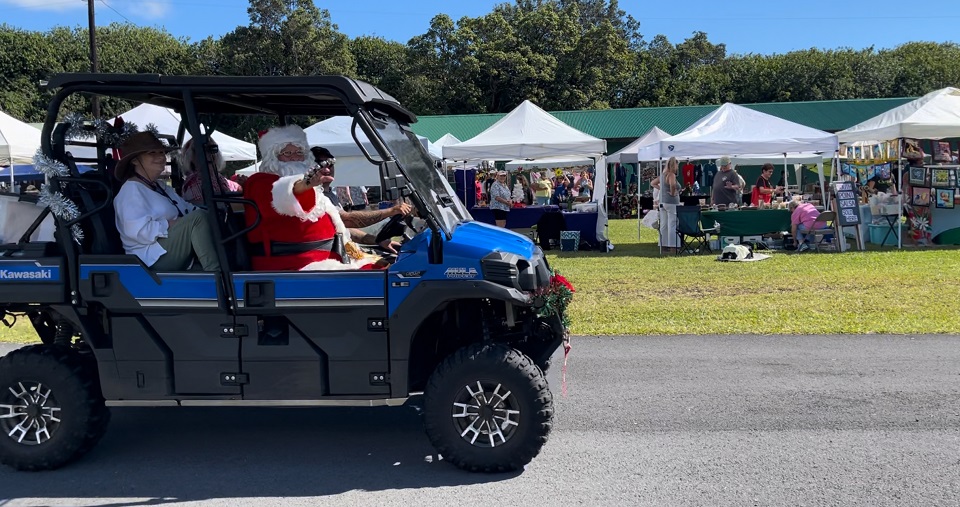 Santa Claus rides shotgun in a blue all terrain vehicle with passengers