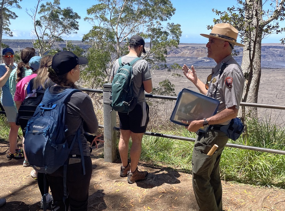 A park ranger holds photographs and talks with visitors at the edge of a volcanic crater