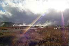 Sunlight streams through the clouds along the roadway with steaming vents in the background.