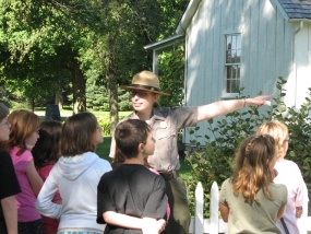 A ranger points out a small white house to elementary school children.