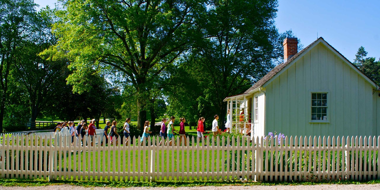 A line of school children enter a small historic home.