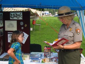 A park ranger quizzes a little girl at an activity table.