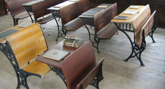Slates and readers adorn the top of antique wood and iron pupils' desks.