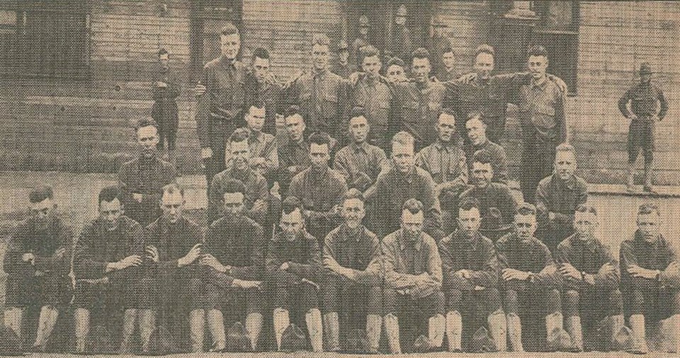 Several men standing and sitting for a group portrait in front of a wooden building