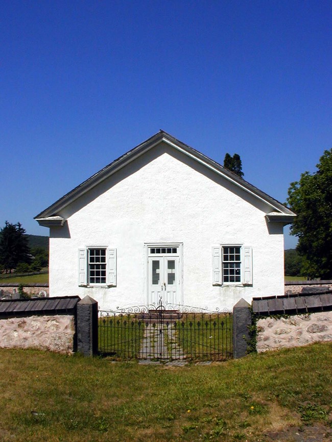 White stone church stands behind stone wall.