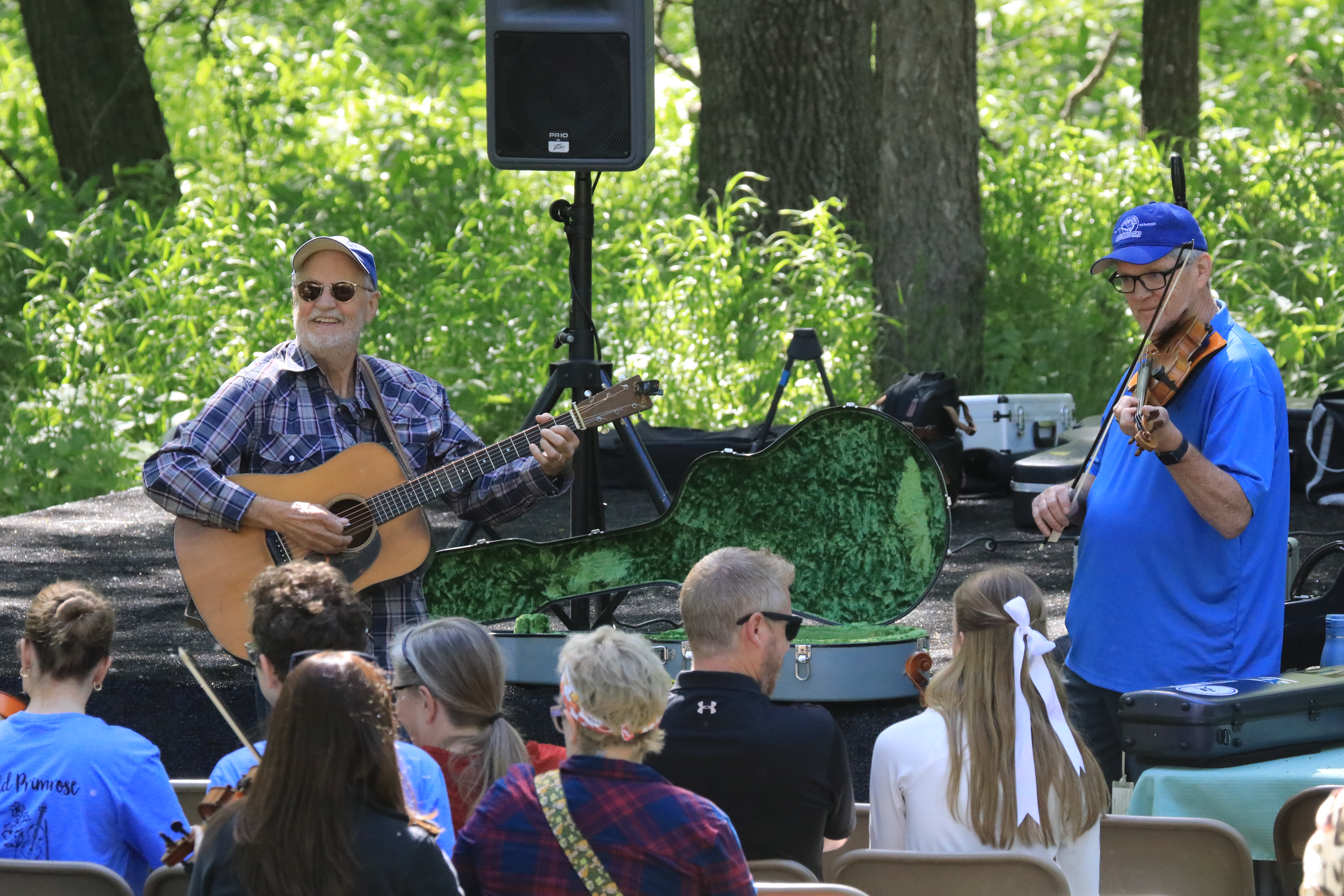 Two guys playing a guitar and fiddle in front of a crowd.