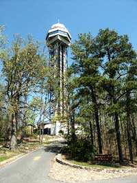 Color photo of steel tower, looking from driveway below tower, spring season with trees half leafed out.