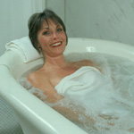 Smiling woman in ceramic tub with water; woman is draped with a white towel