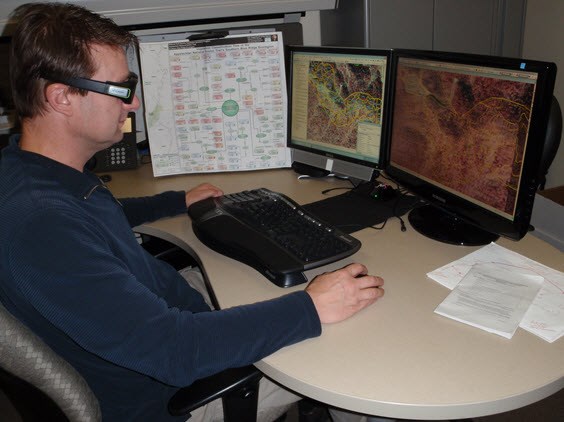 Technician in front of computer monitors using 3-D glasses to view maps