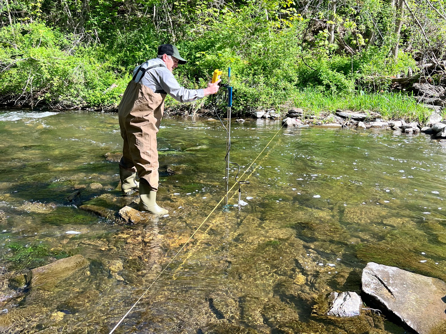 An NPS tech stands in a shallow stream with wq monitoring equipment