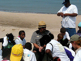 Students listening to a park ranger while kneeling on the beach