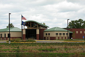 one story building with a tall entrance, green roof and parking lot in front of building